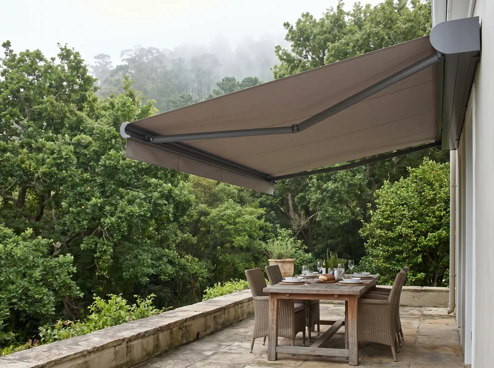 Folding-arm awning extended over a stone patio dining table in a Newlands garden, misty forest canopy overhead